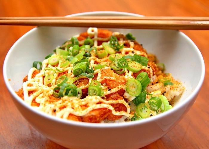 White bowl of breaded meat with seasoning, mayonnaise and green onions, chopsticks on bowl
