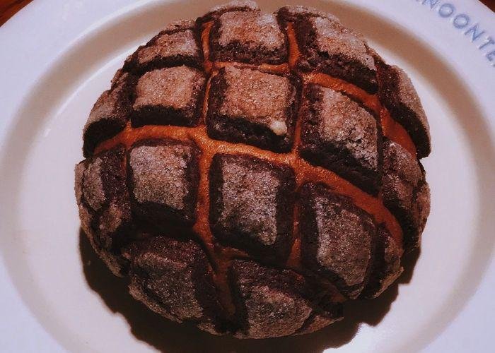 This melon pan is a dark brown color. The top is a crunchy layer in a checkered pattern.