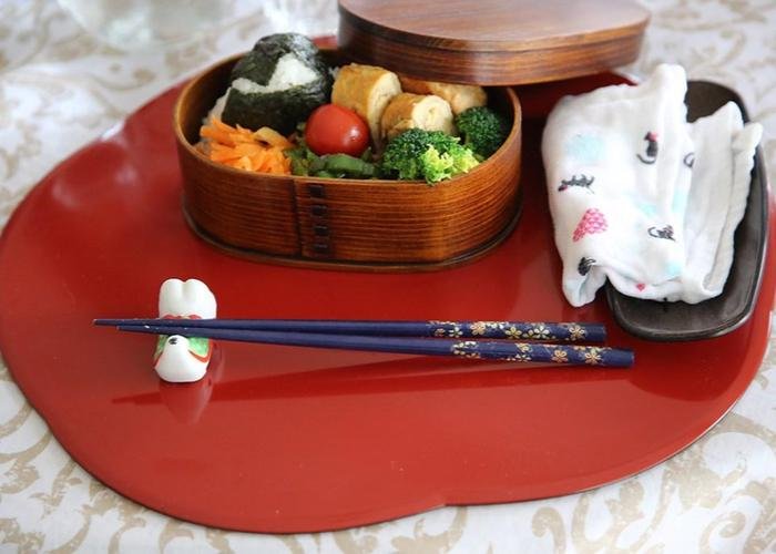 A wooden bento box packed with colorful vegetables and rice, with chopsticks resting in front. 