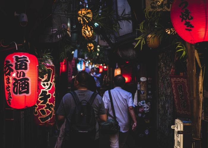 Men walking through a Tokyo Yokocho drinking alley with glowing red lanterns