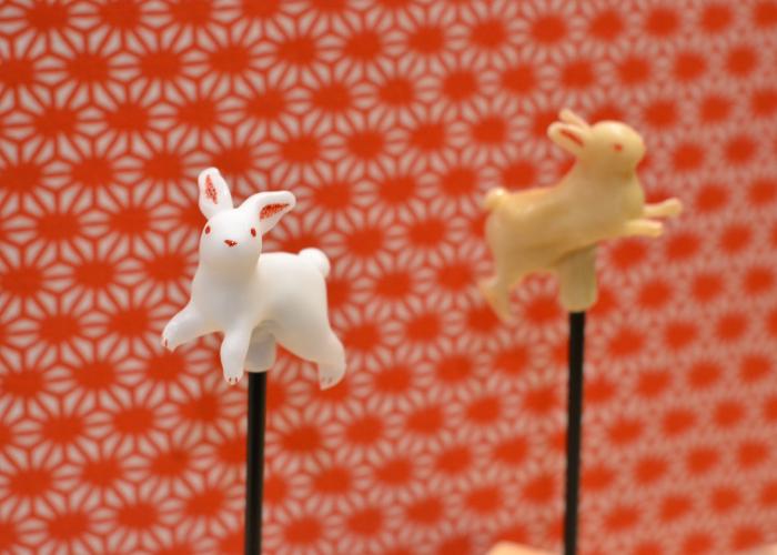 Two Japanese amezaiku candy rabbits against a red backdrop 