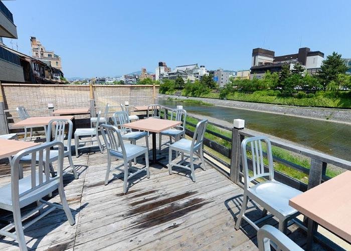 A wooden outdoor patio, filled. with chairs and tables, with the river visible over the barrier.