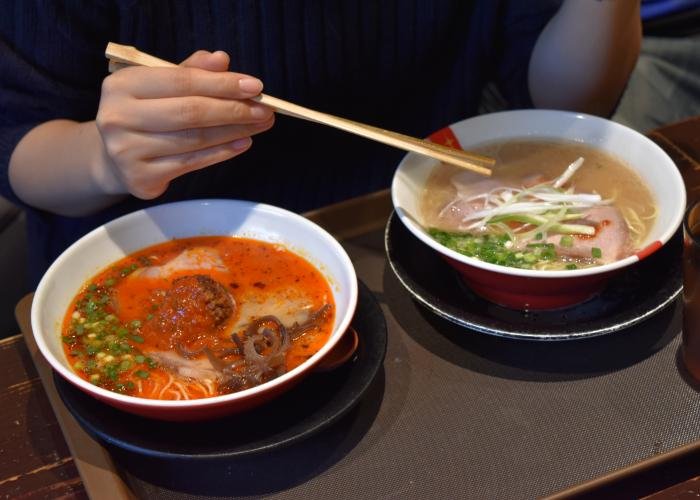 Two mini bowls of ramen, one with a bright red broth, the other with a light-colored broth, during a ramen food tour in Tokyo