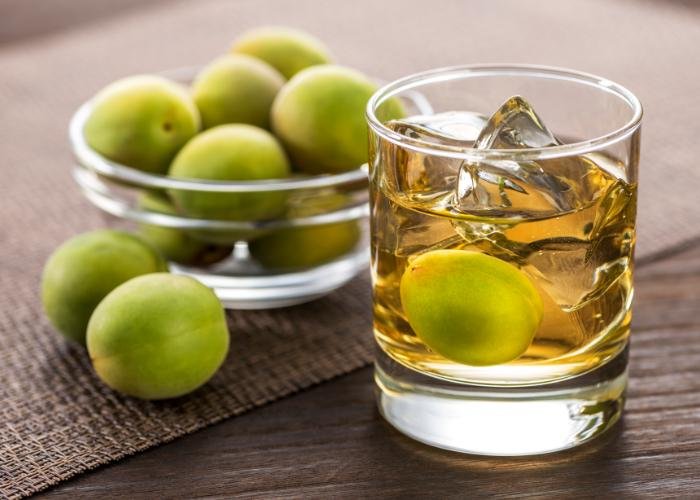 Japanese umeshu plum wine. A bowl of green Japanese ume plums and a cup of amber liquid