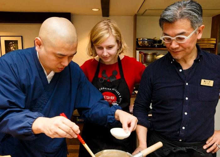 A Japanese cooking instructor shows a couple what to do with their pot of food.