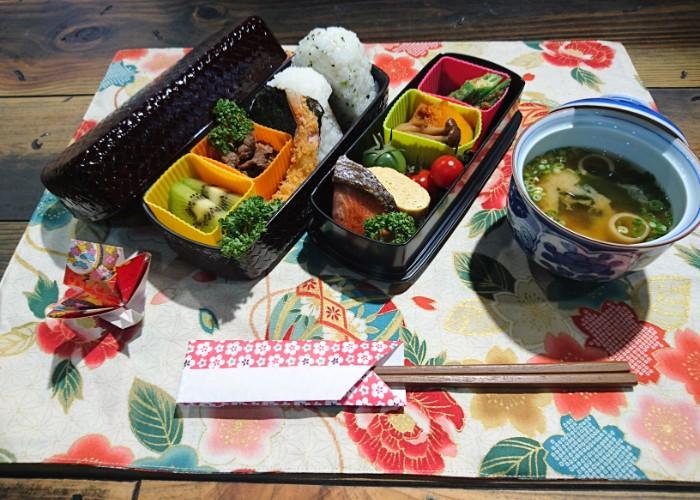 A nicely patterned bento box sits on a table wit its lid off, showing a range of colorful foods stuffed inside.