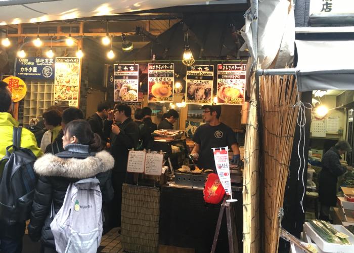 A food stall serving seafood with a crowd of customers at Kizu Market in Osaka