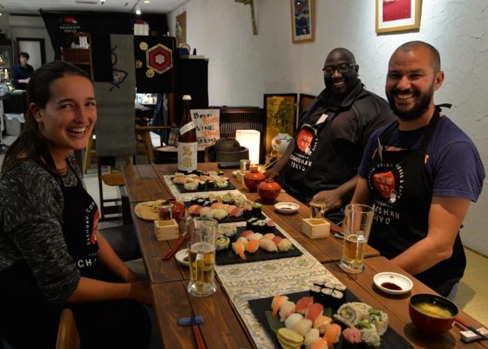 A woman and two men with plates of nigiri sushi in front of them smile during a Nigiri and Rolled Sushi Making Class in Tokyo