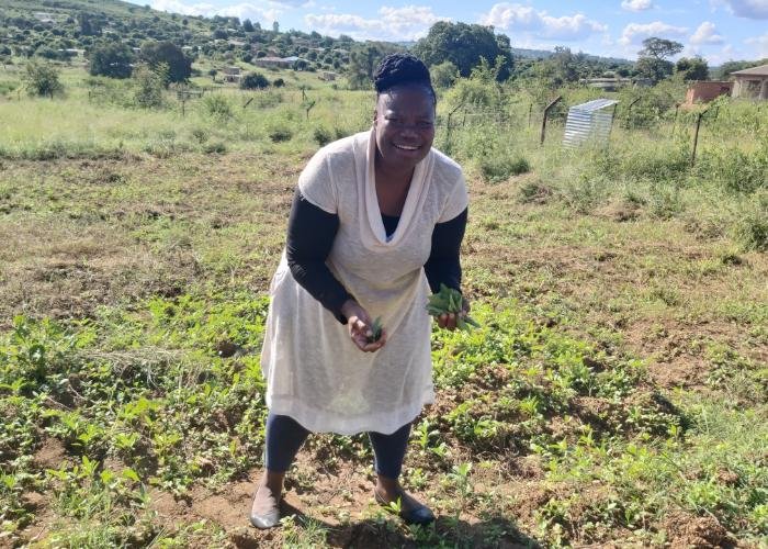 A South African woman stands in a field, smiling and holding vegetables she harvested