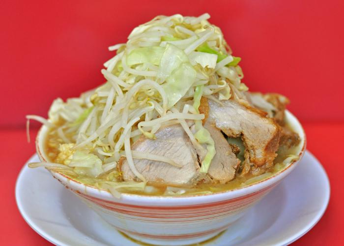 Enormous bowl of ramen at Ramen Jiro, with a towering mound of vegetables against a red backdrop