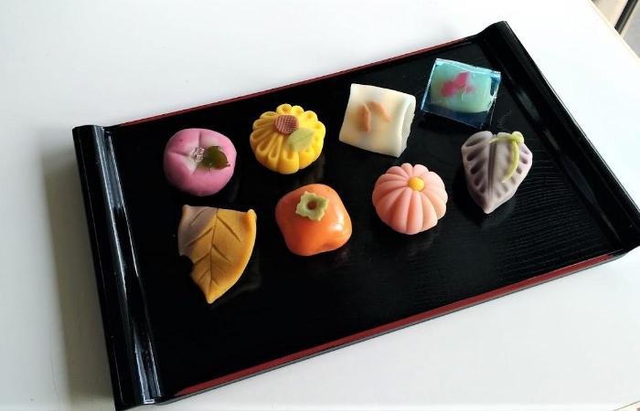 Eight types of wagashi (Japanese sweets) on a black platter, shaped into designs like a persimmon and flowers