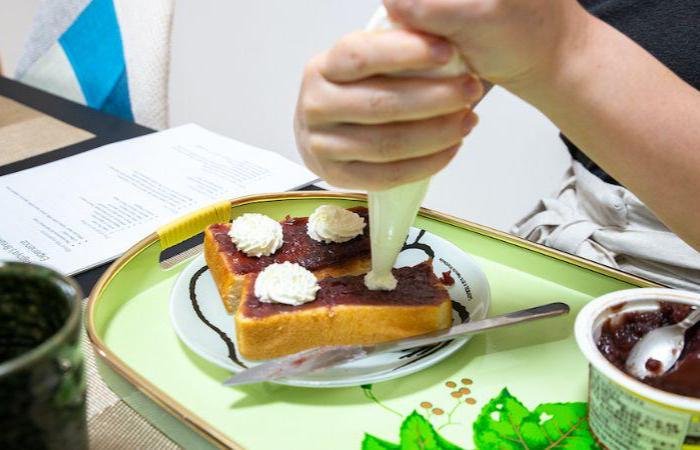 Two hands making Ogura toast, a Nagoya specialty consisting of bread with a layer of red bean paste and whipped cream