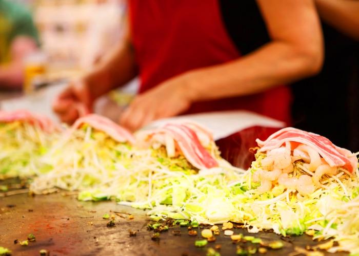 Hiroshima style okonomiyaki being grilled on the teppan