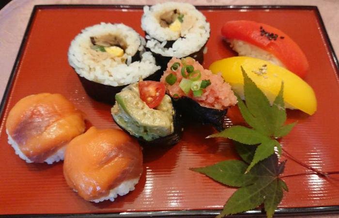 8 pieces of sushi (topped with red and yellow fish, rolled, topped with wasabi and roe) on red square plate with leaves