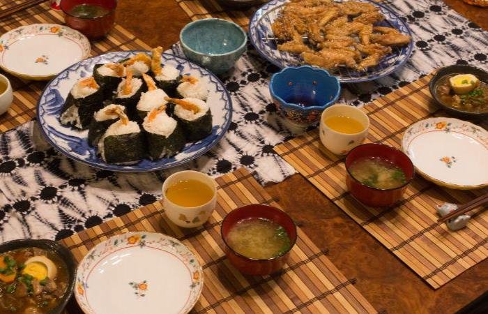 Tebasaki chicken wings and tenmusu tempura sushi spread on Japanese dishware with bowls of tea and miso