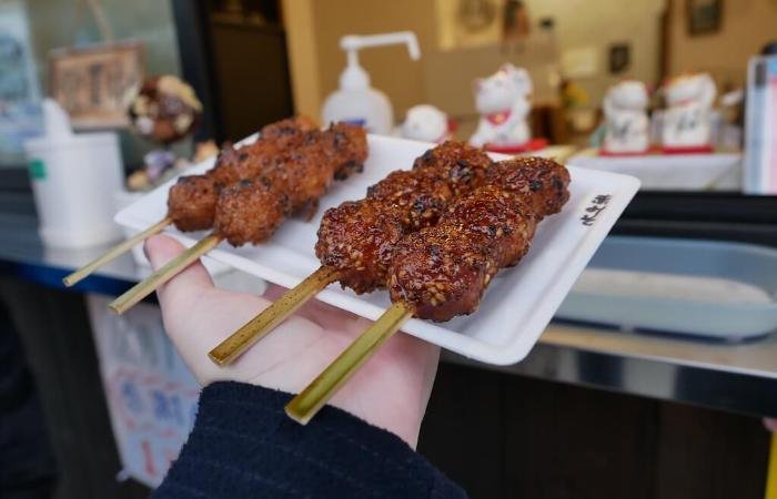 Several skewers of meat with dark brown sauce on plate with maneki neko statues on window in background