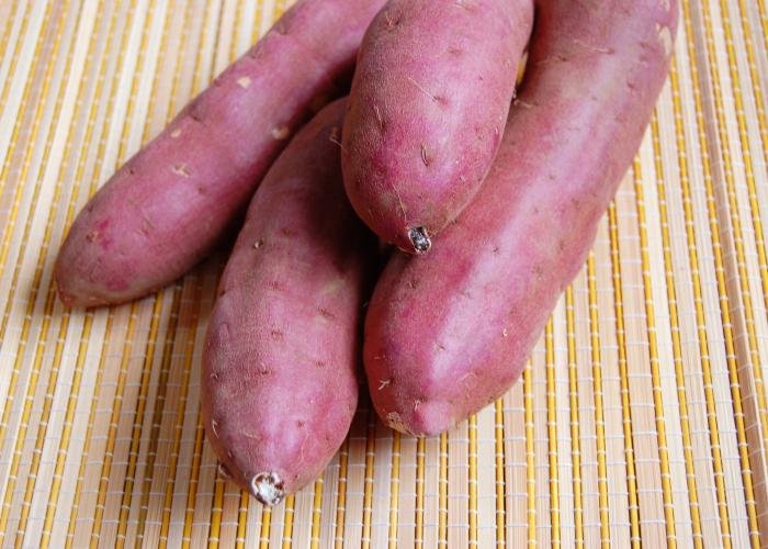 Four raw reddish-purple Satsuma-imo Kagoshima sweet potatoes on a light yellow mat