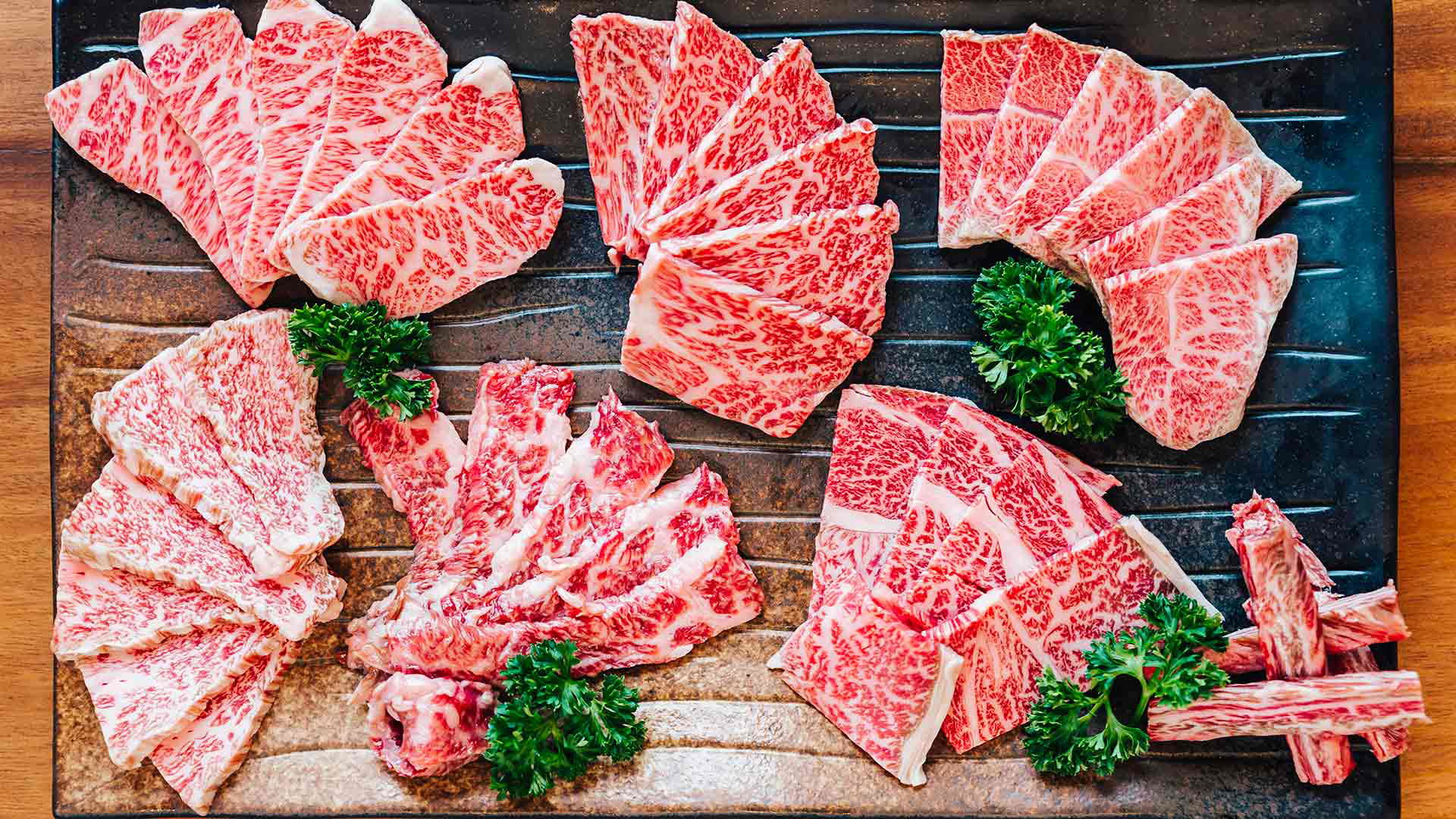 Variety of marbled Wagyu beef slices with garnish on wooden tray