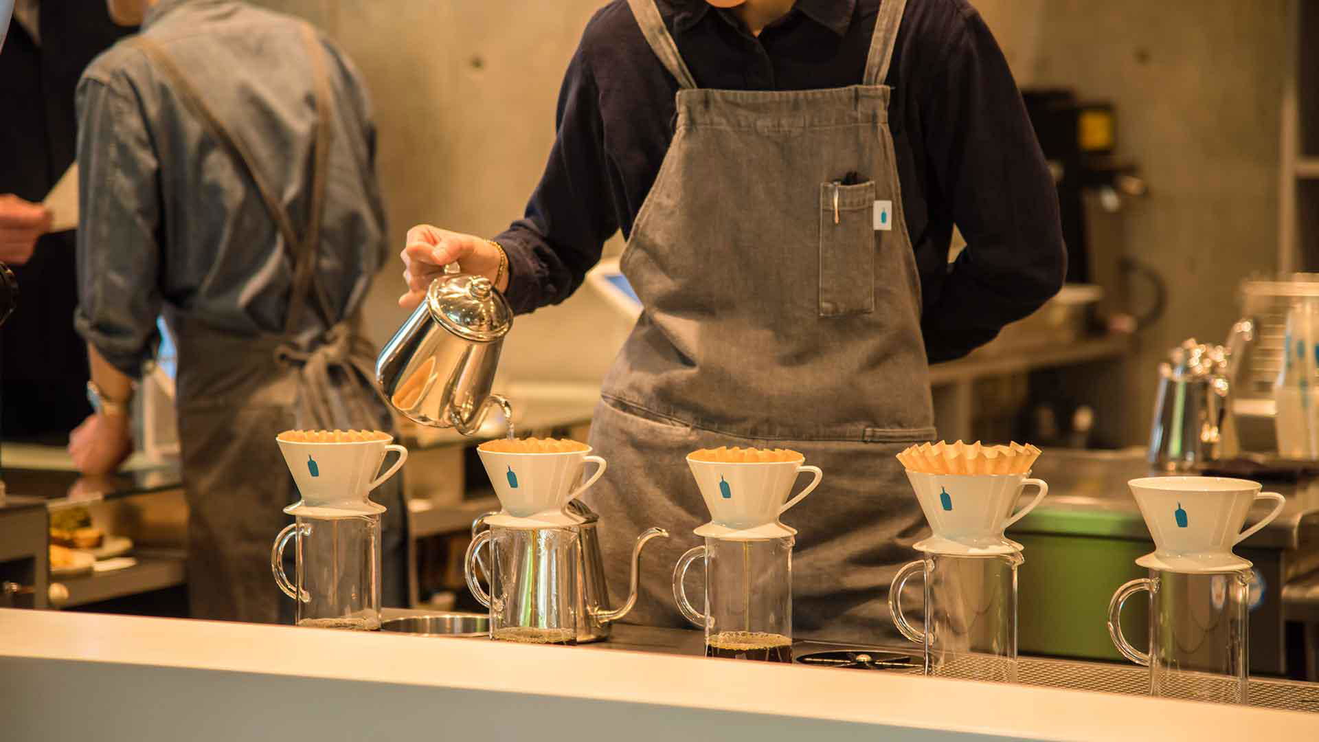 Barista brewing coffee using drip filters in a trendy café setting