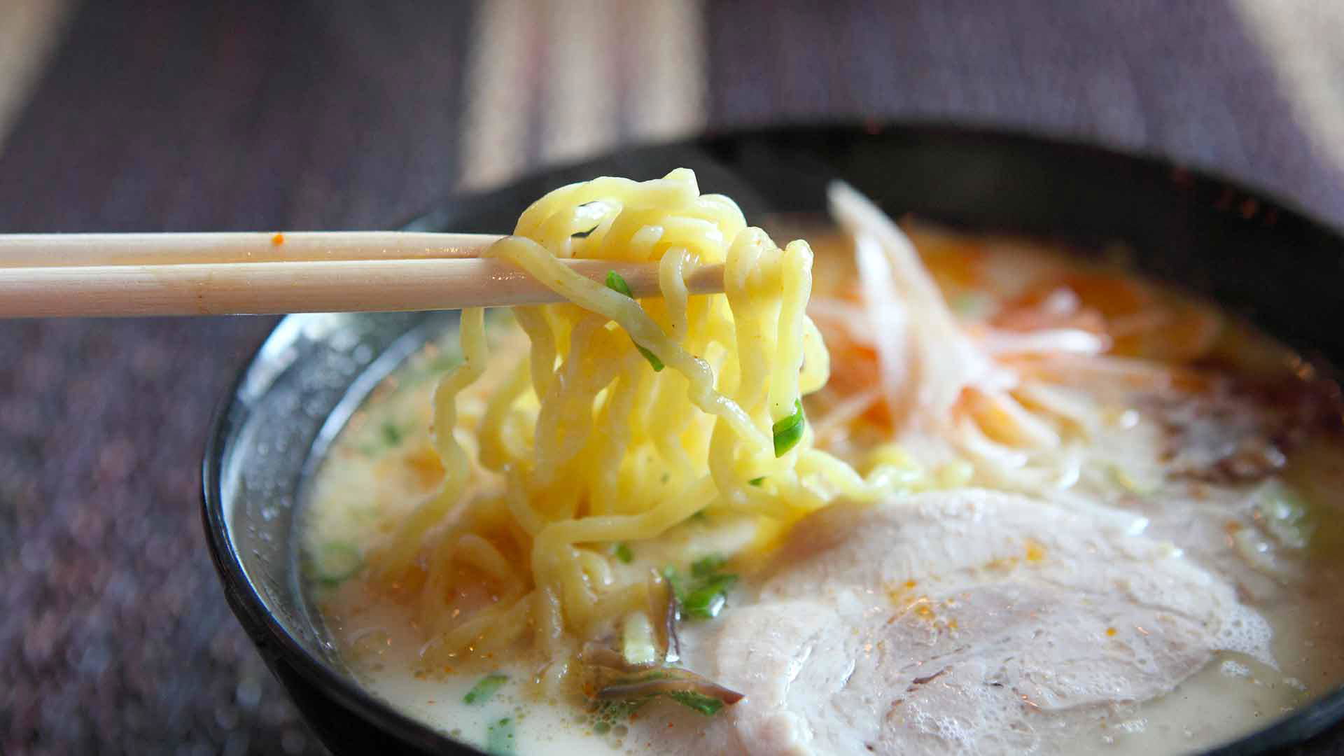 Bowl of ramen with chopsticks lifting noodles