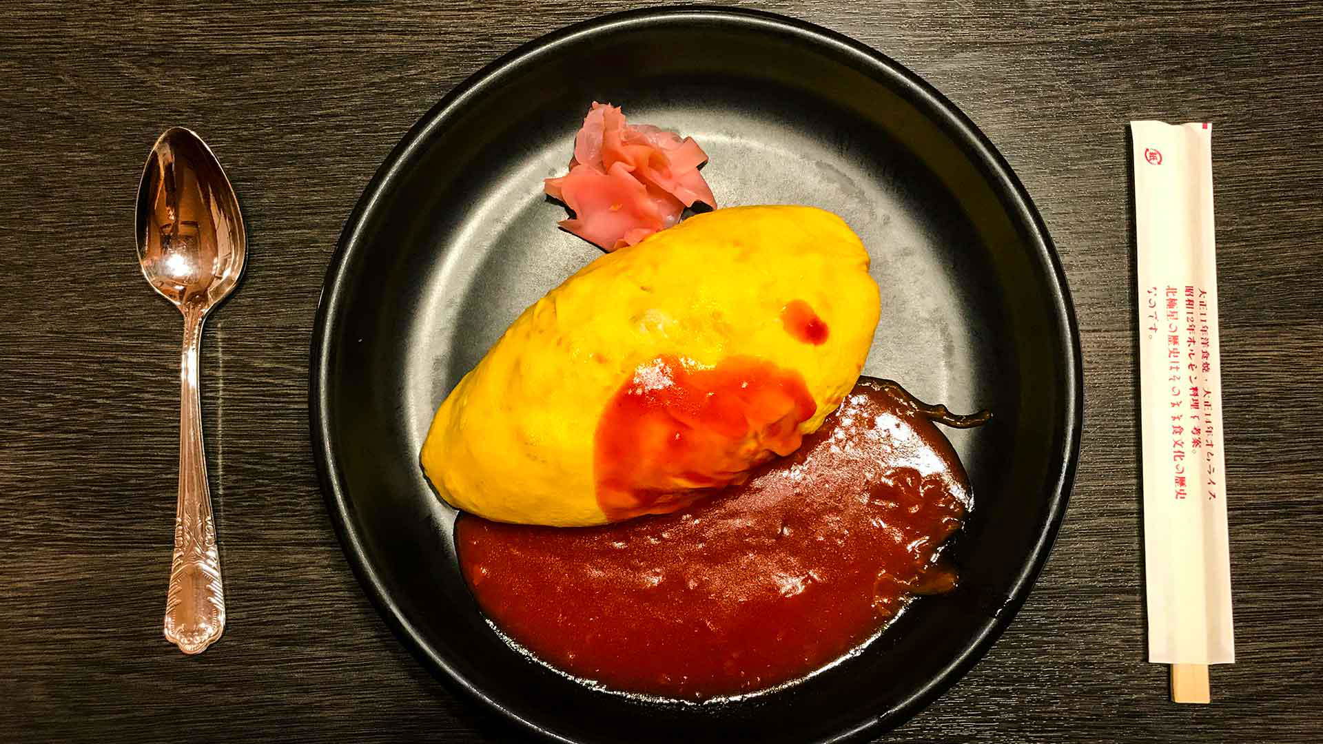 Japanese omelette rice with sauce and pickled ginger on black plate
