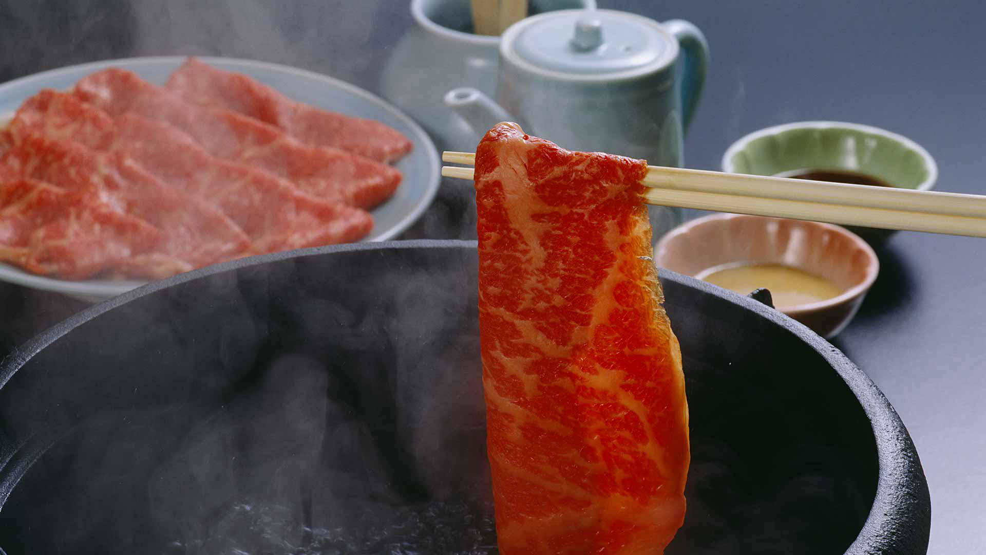 Cooked beef slice on chopsticks over a steaming hot pot