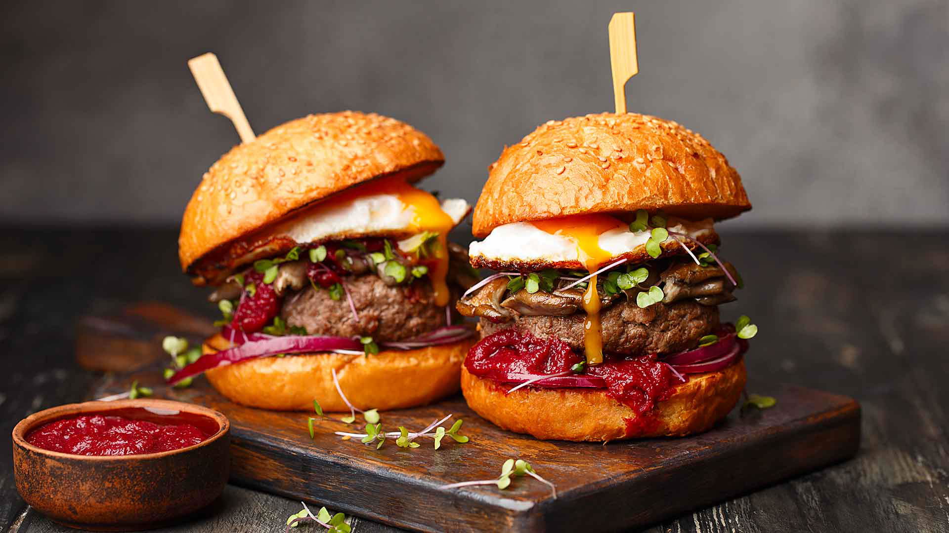 Gourmet beef burgers with fried egg and microgreens on a wooden board
