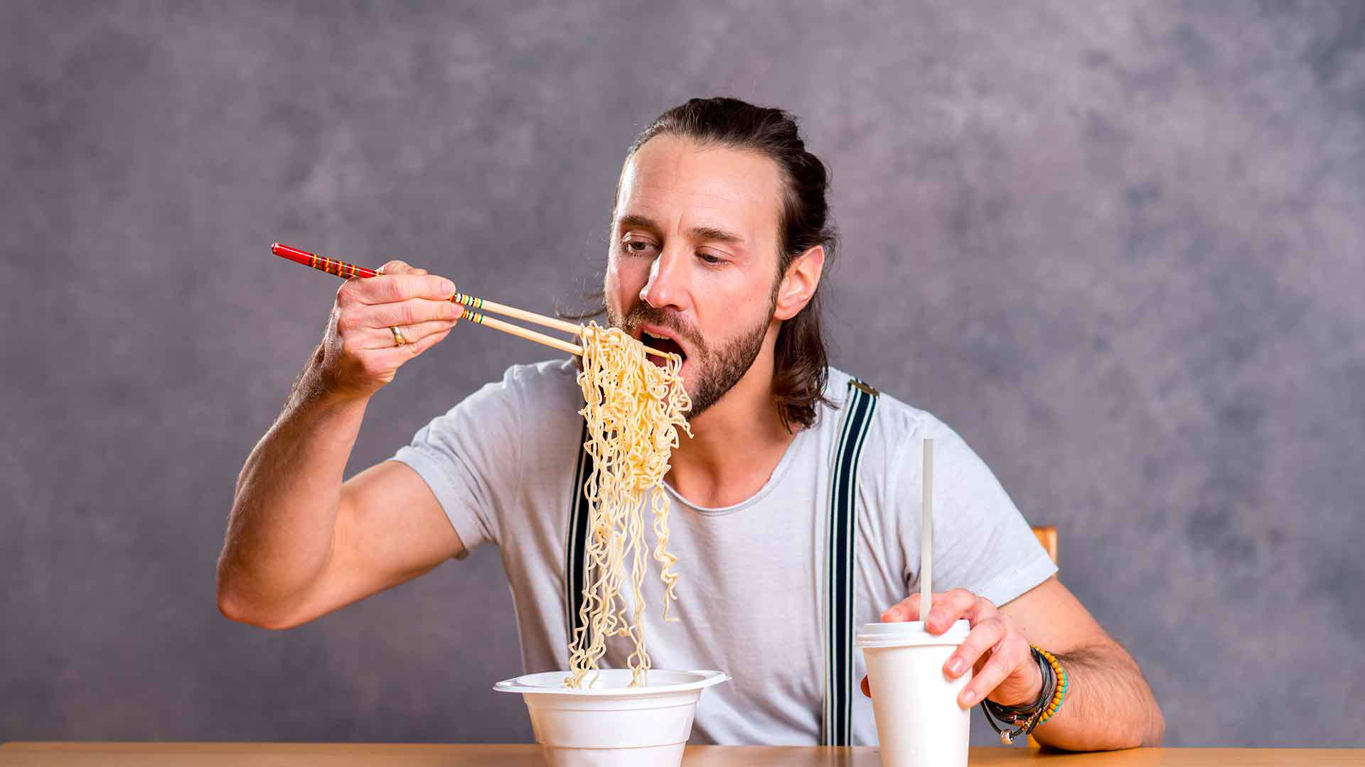 Man enjoying instant noodles with chopsticks and takeaway coffee