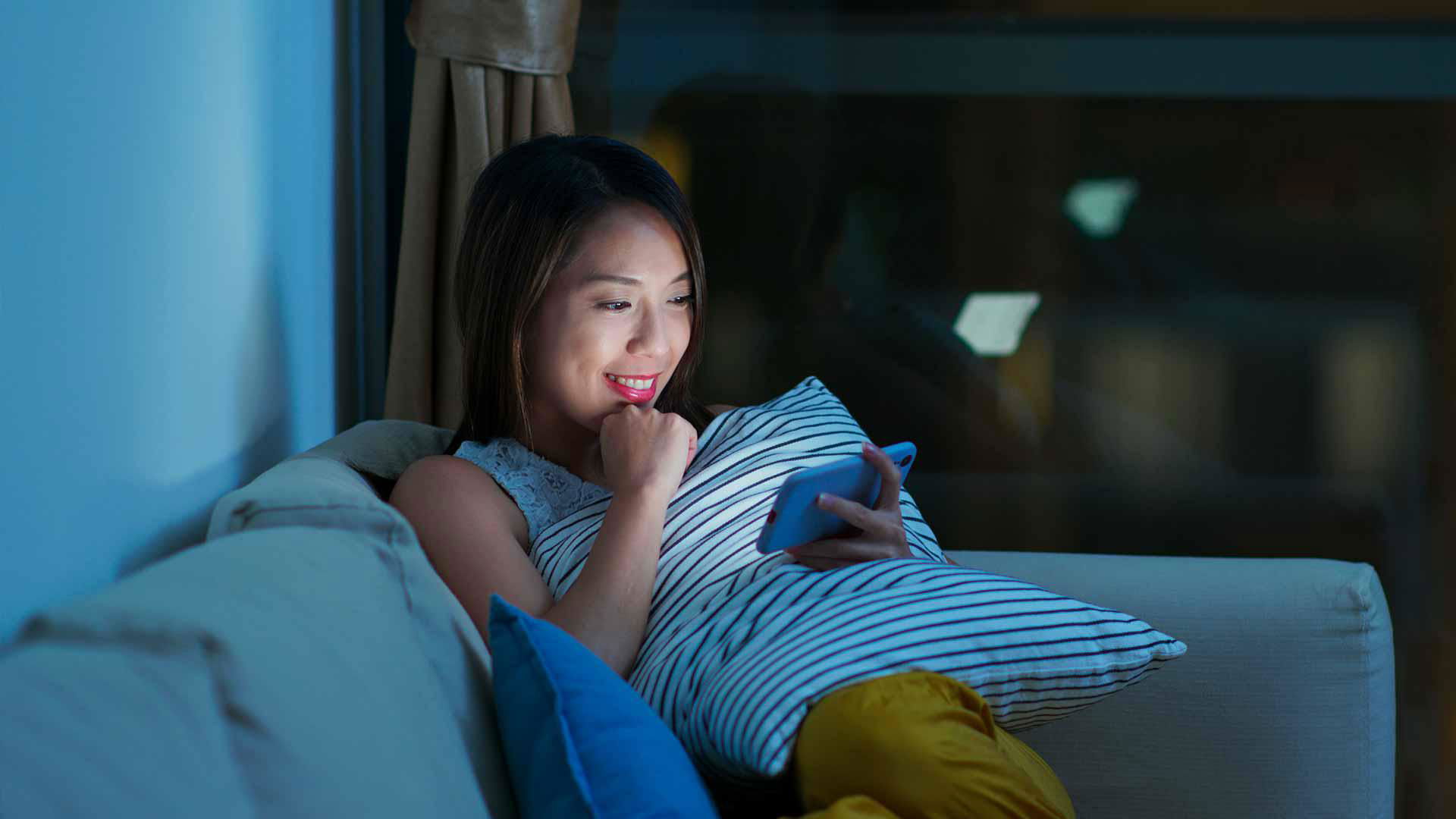 Woman smiling while using smartphone on couch at night